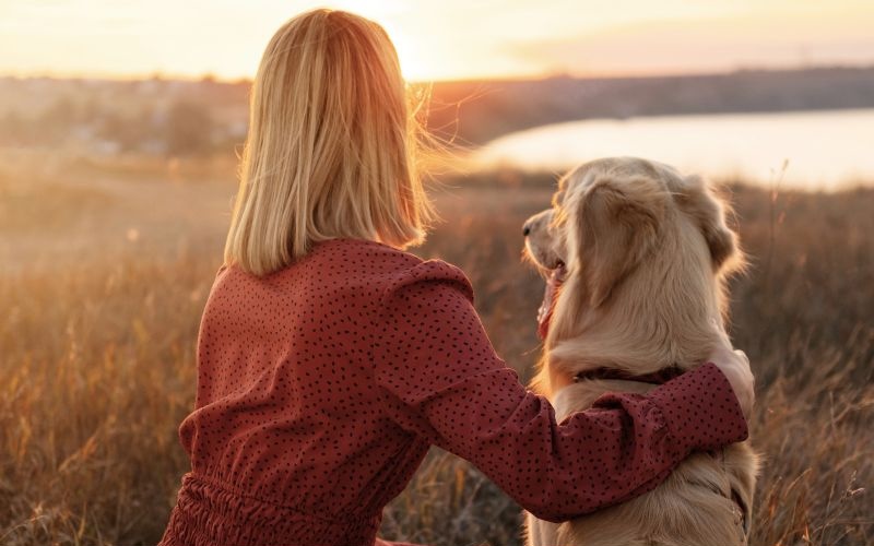 Woman and dog sitting outside at sunset